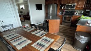 Cozinha moderna com armários de madeira, eletrodomésticos de aço inoxidável e uma área de jantar com uma mesa grande de madeira e cadeiras.
