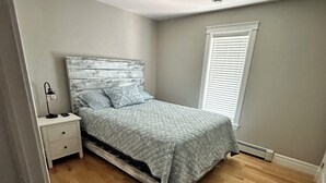 Quarto com cama, mesa de cabeceira e janela com persianas.