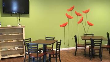 A dining area with wooden tables and chairs, a flat-screen TV mounted on the wall, and a bookshelf with various items.