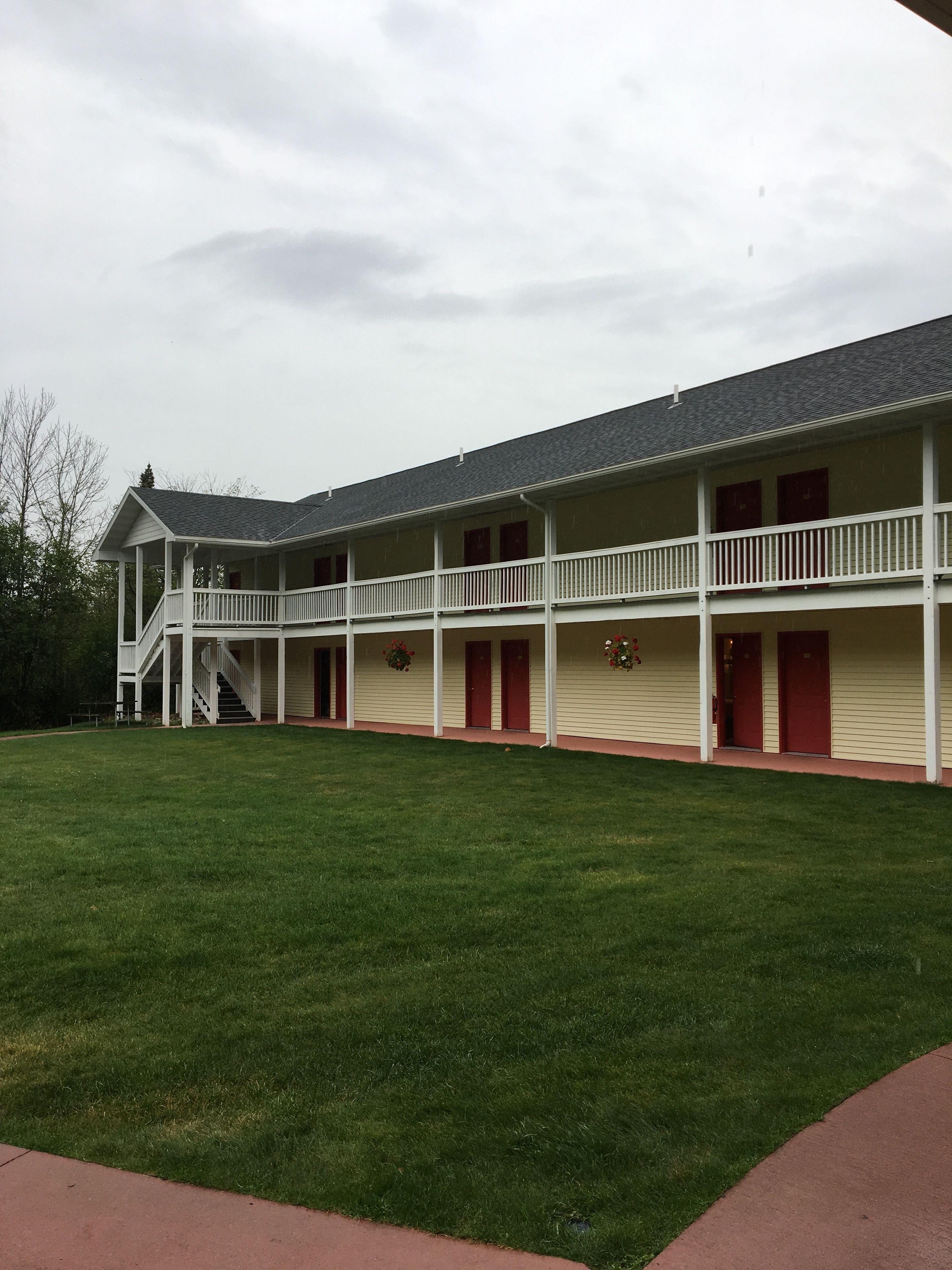 A two-story building with a covered walkway and a grassy lawn.