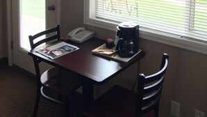 A small dining area with a table, chairs, a coffee maker, and a window with blinds. - The Beach Inn Motel (Munising)
