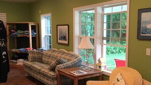 A living room with a plaid sofa, a yellow armchair, a wooden table, and a window with a view of greenery. - The Beach Inn Motel (Munising)