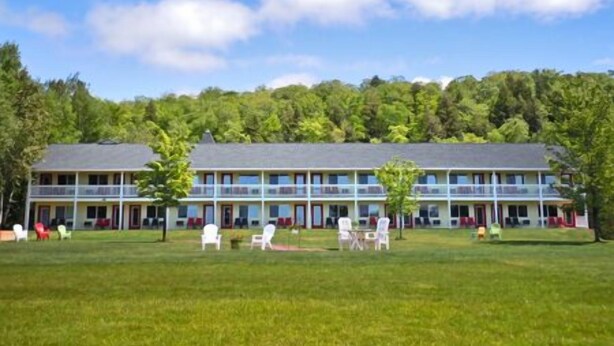 A two-story building with a flat roof, surrounded by a grassy lawn and trees. - The Beach Inn Motel (Munising)