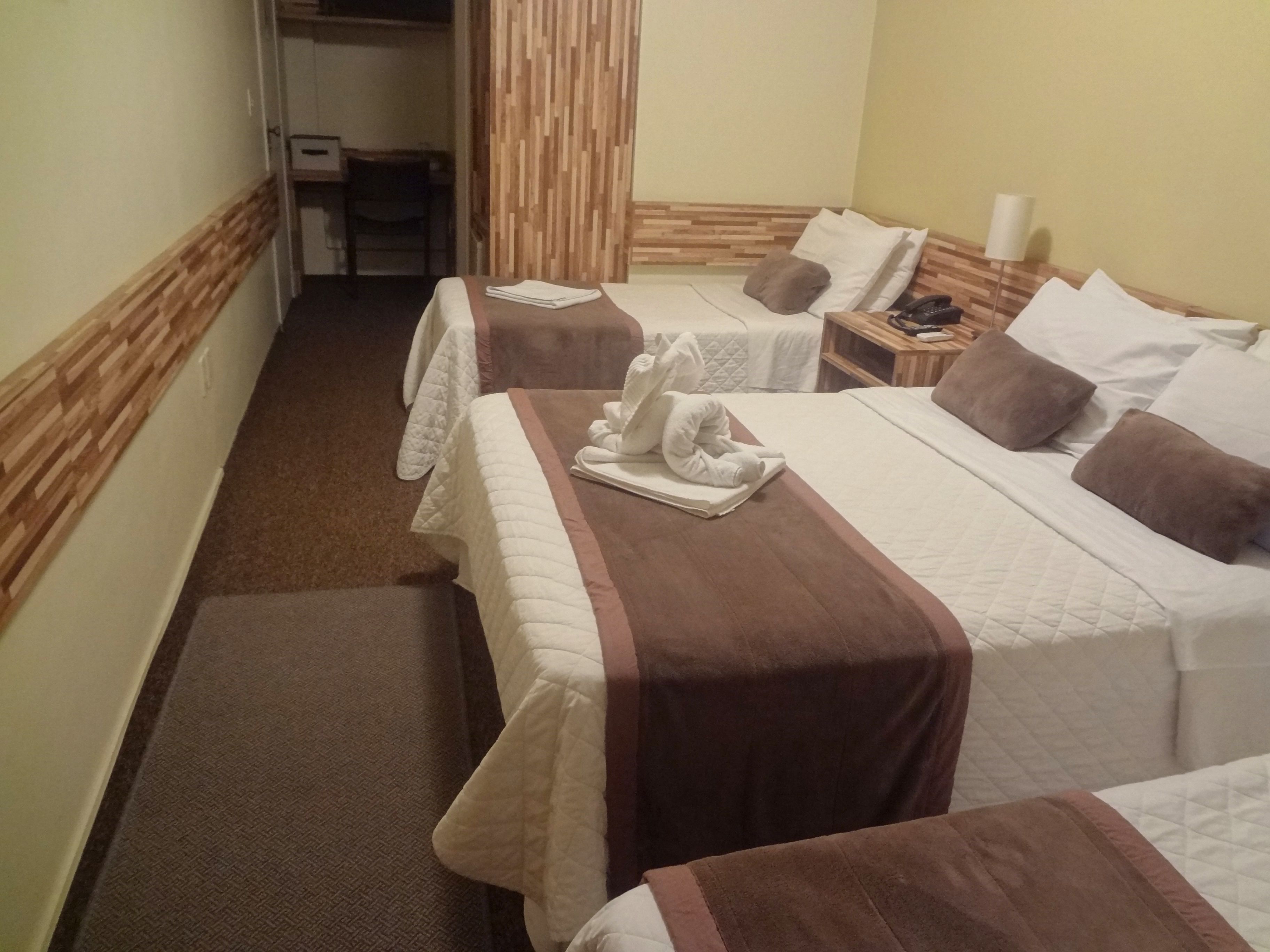 Une chambre d’hôtel avec deux lits, chacun doté d’une tête de lit marron, de draps blancs et d’une serviette posée sur le lit. On y trouve une table de chevet en bois avec une lampe et un téléphone.