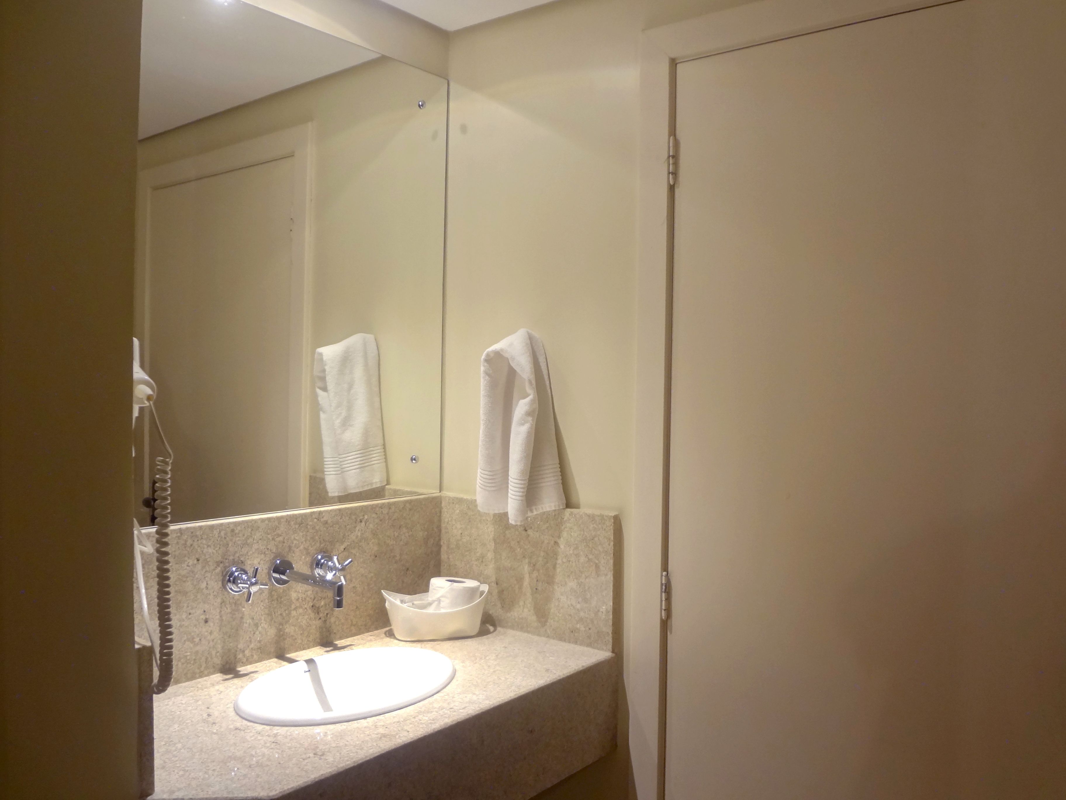 Et badeværelse med vask, spejl, håndklædestige og toiletpapirsholder.