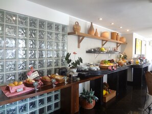 A breakfast bar with various food items, a glass block wall, and shelves with pottery. - Novo Hamburgo Business Hotel (Novo Hamburgo)