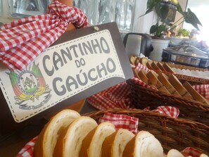 A sign reading "Cantinho do Gaúcho" with a logo, and a basket of sliced bread. - Novo Hamburgo Business Hotel (Novo Hamburgo)
