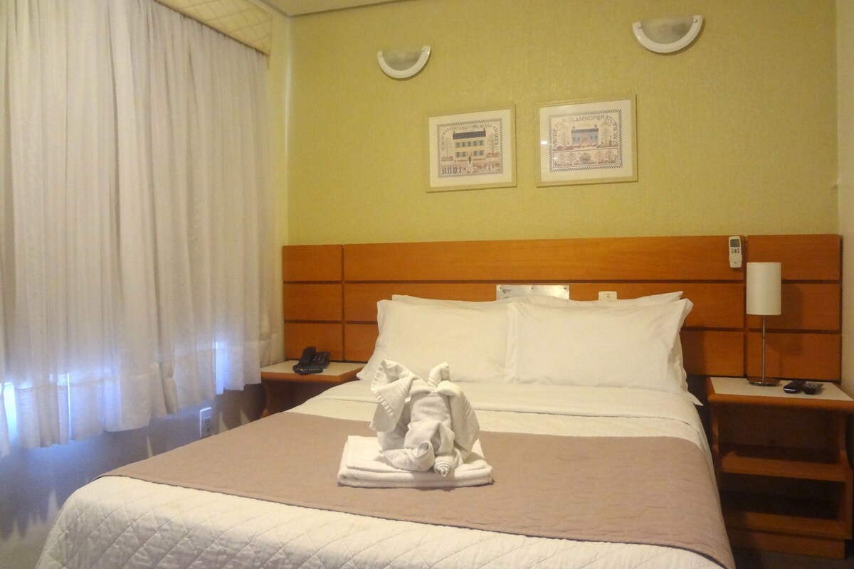 A hotel room with a bed, a nightstand, a lamp, and two framed pictures on the wall.