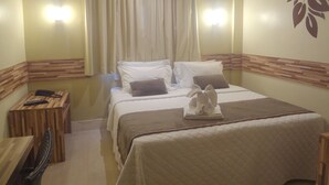 A hotel room with a bed, a wooden side table, a telephone, and a wall-mounted air conditioner. - Novo Hamburgo Business Hotel (Novo Hamburgo)