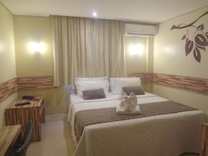 Habitación de hotel con cama, mesita de noche de madera, teléfono y aire acondicionado instalado en la pared.