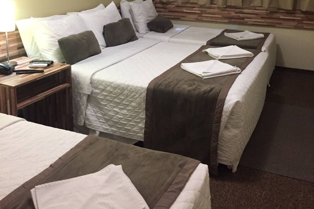 A hotel room with two beds, a nightstand, a lamp, and a window with curtains.
