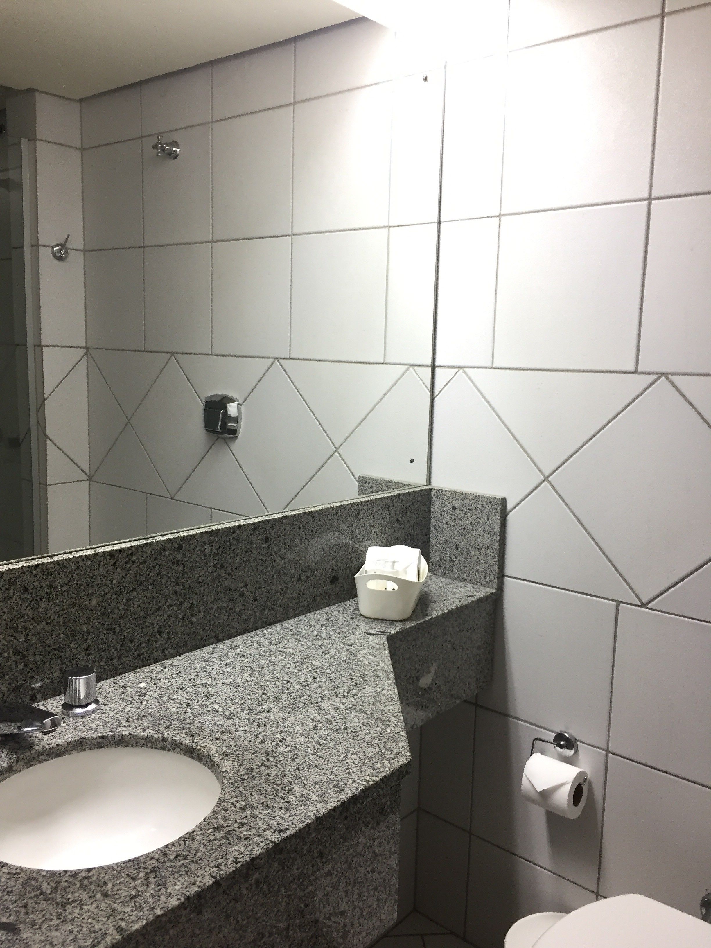 Un baño con lavamanos de encimera de granito, un espejo, dispensador de toallas y un inodoro.