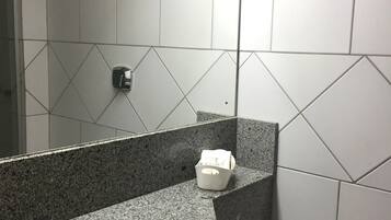 Un baño con lavamanos de encimera de granito, un espejo, dispensador de toallas y un inodoro.