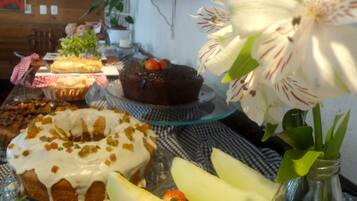 Ein Tisch mit verschiedenen Desserts, darunter ein Kuchen mit Erdbeeren, ein Donut mit weißem Zuckerguss und ein Schokoladenkuchen mit einer Erdbeere obenauf. Außerdem steht eine Vase mit weißen Blumen und eine Glasflasche darauf.