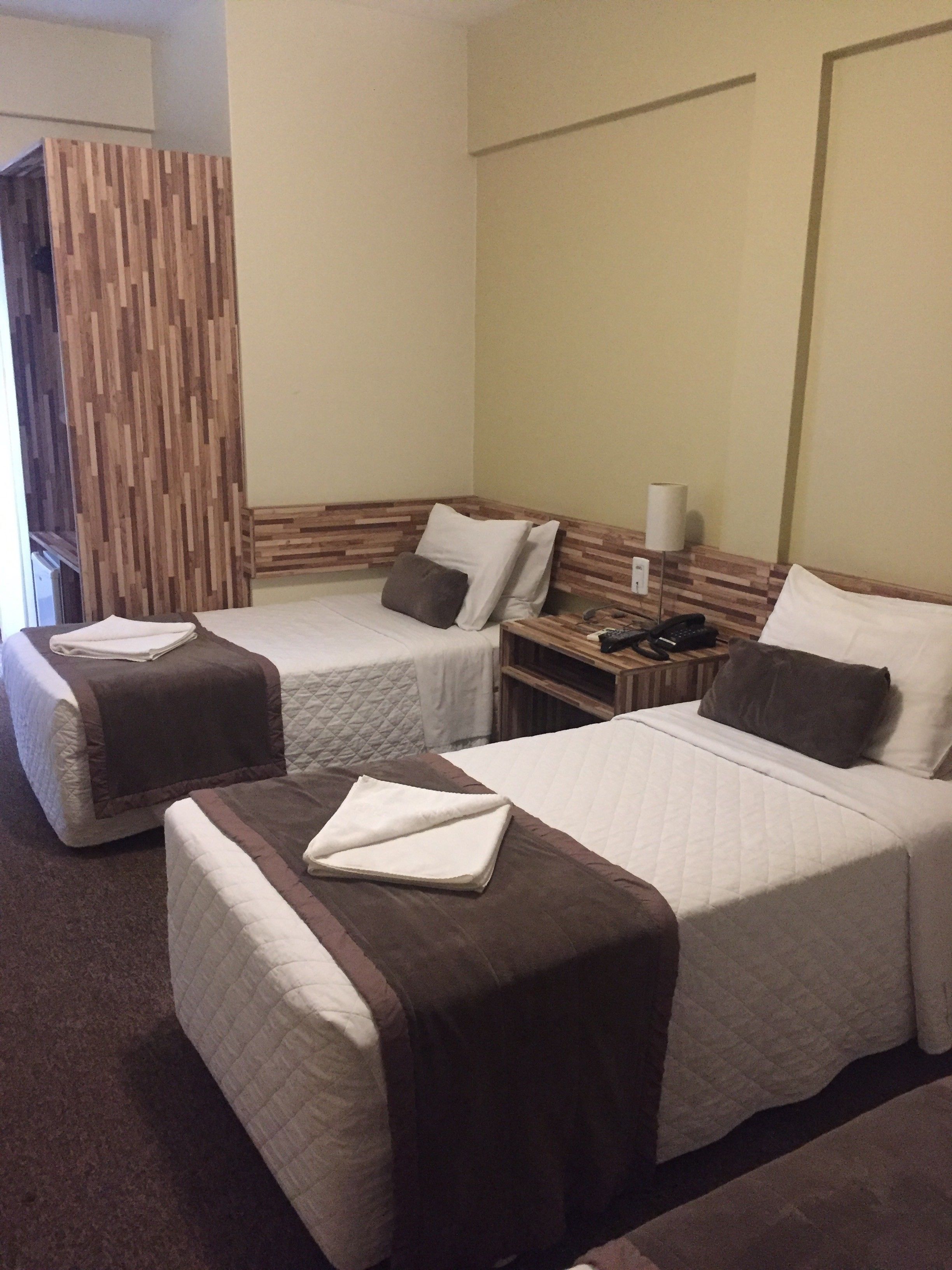 A hotel room with two single beds, a wooden headboard, a bedside table with a lamp, and a wall-mounted telephone.