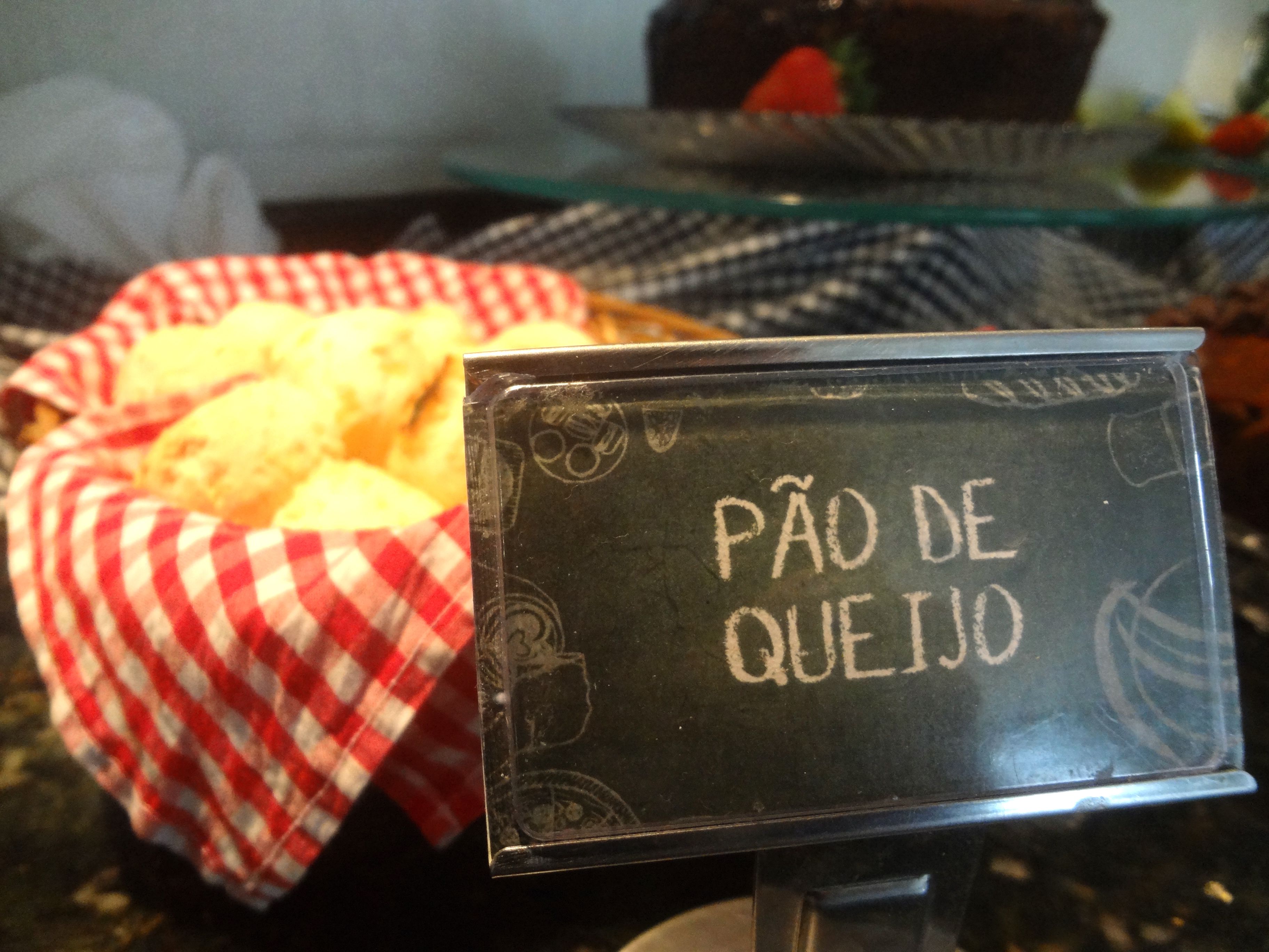 A sign reading "PÃO DE QUEIJO" with a basket of bread in the foreground.