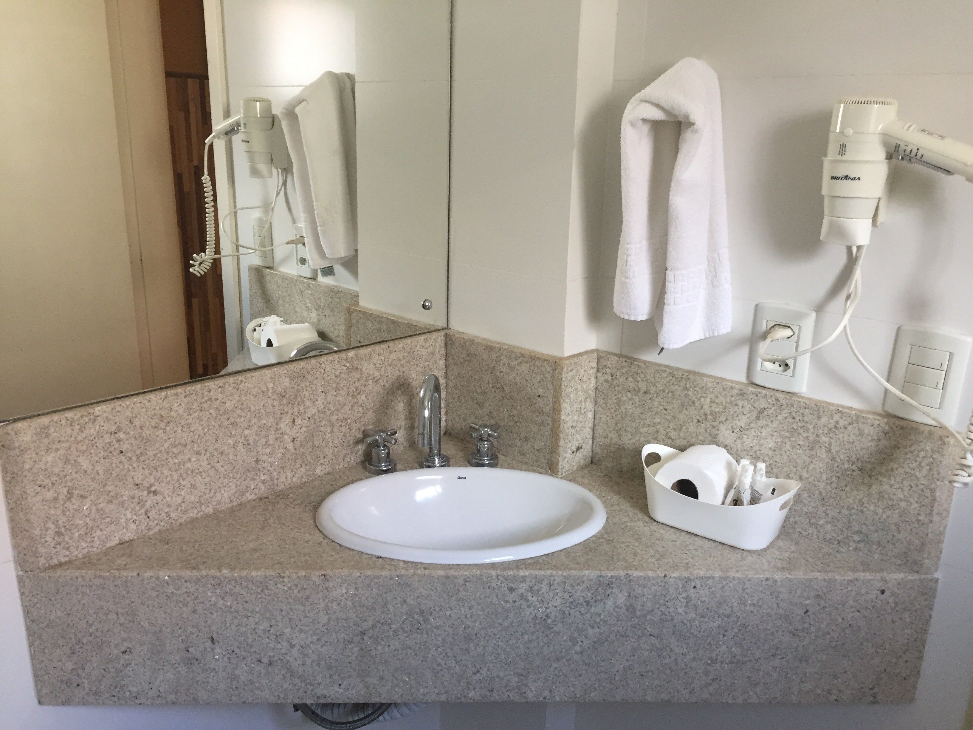 A bathroom with a granite countertop, a white sink, a mirror, a towel rack, and a hairdryer.