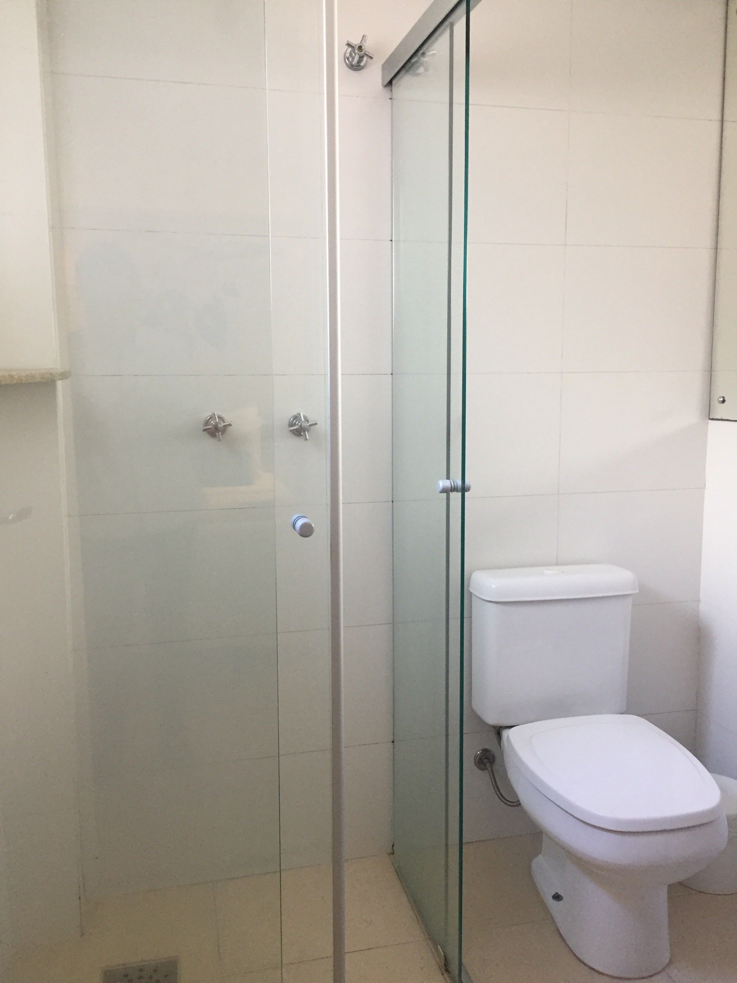 Un baño con ducha de vidrio, inodoro blanco y suelo de baldosas.