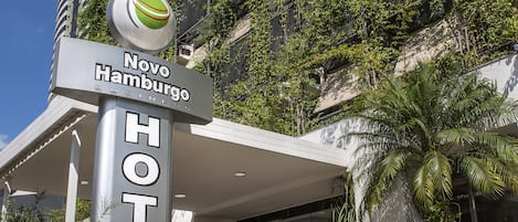 A hotel entrance with a sign for Novo Hamburgurgo Hotel, featuring a modern design with a covered entrance and potted plants.