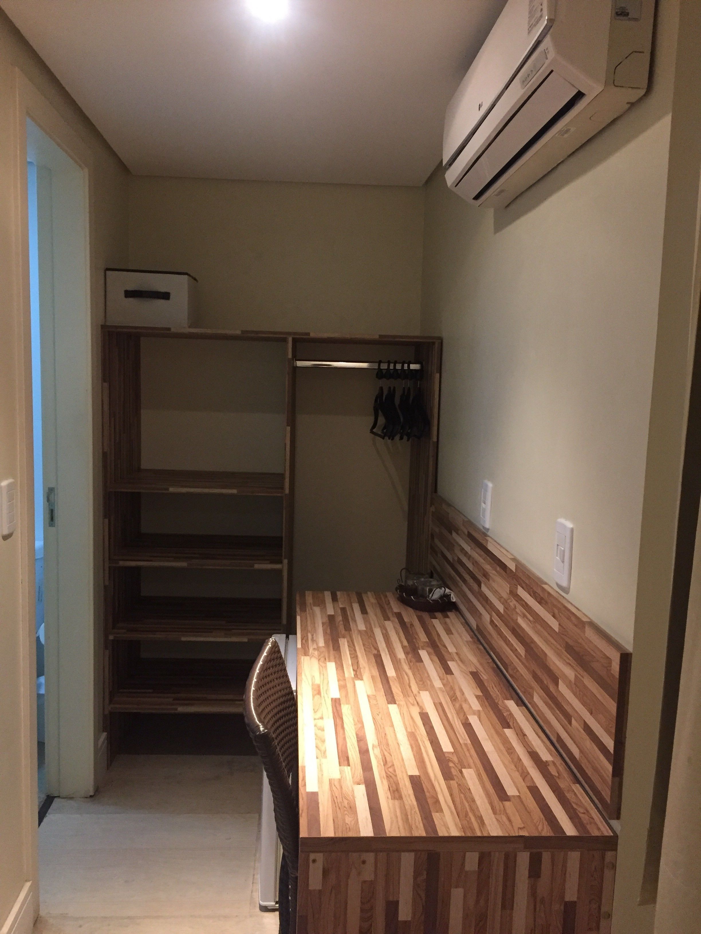 A compact room with a built-in wardrobe, a wooden dining table, and a ceiling-mounted air conditioner.