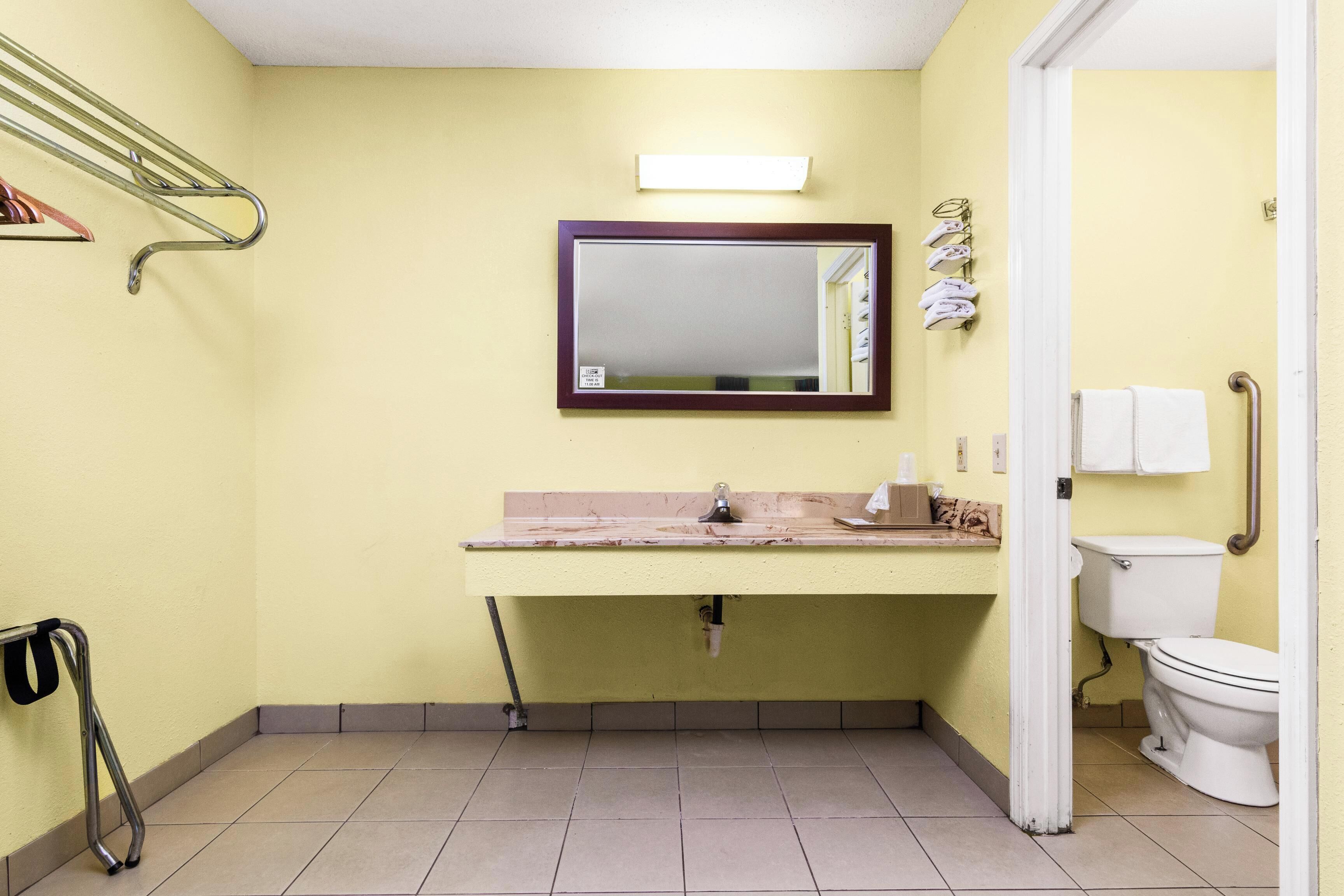 Un baño pequeño con pared amarilla, espejo, lavamanos, inodoro y zona de ducha.