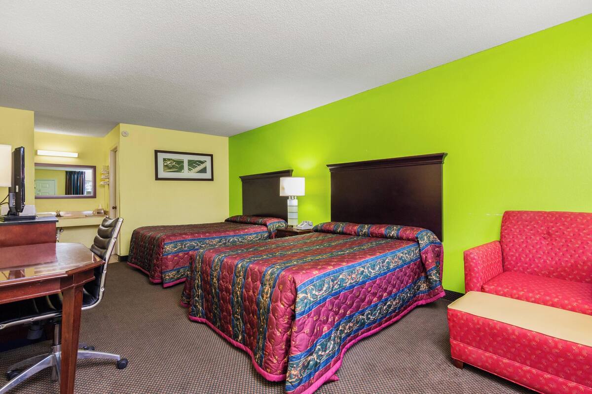 A hotel room with two beds, a desk, a chair, and a red sofa.