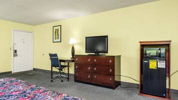 A hotel room with a bed, a desk with a chair, a television, a dresser, and a refrigerator.