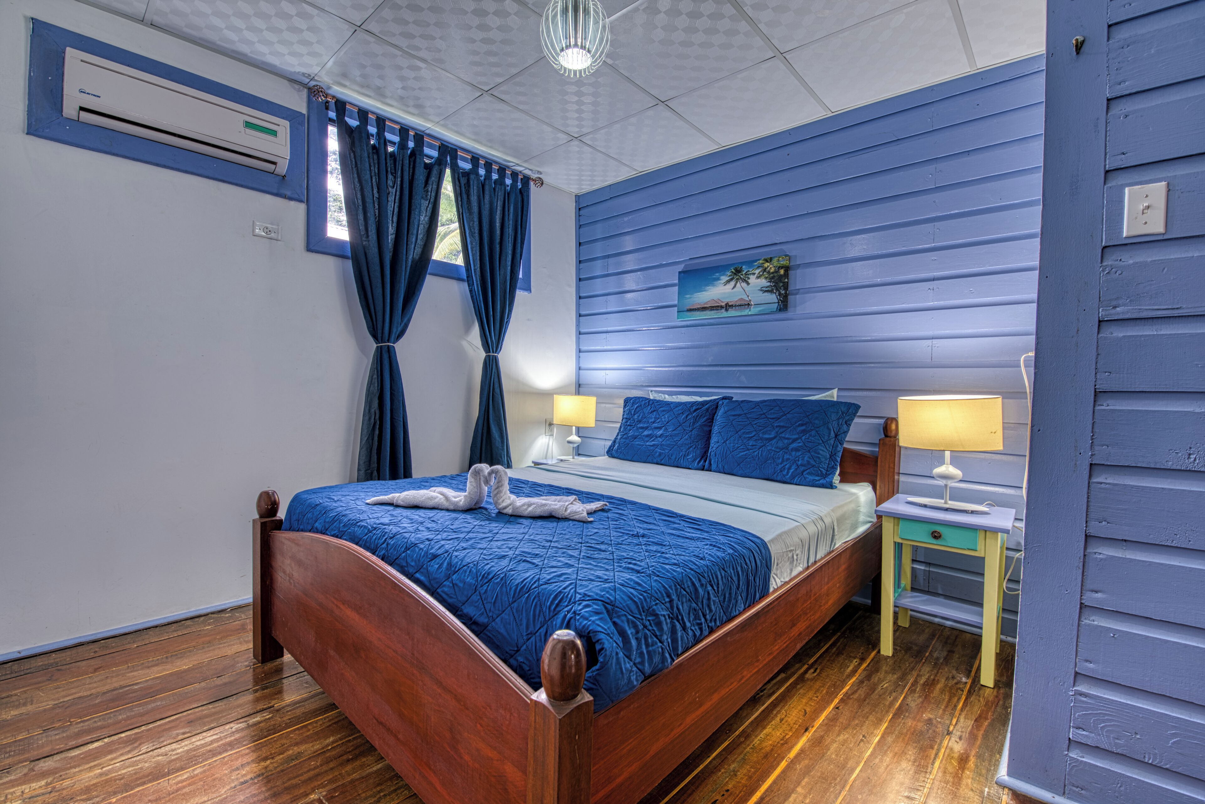 Quarto com cama de madeira, mesa de cabeceira, abajur e um quadro na parede.