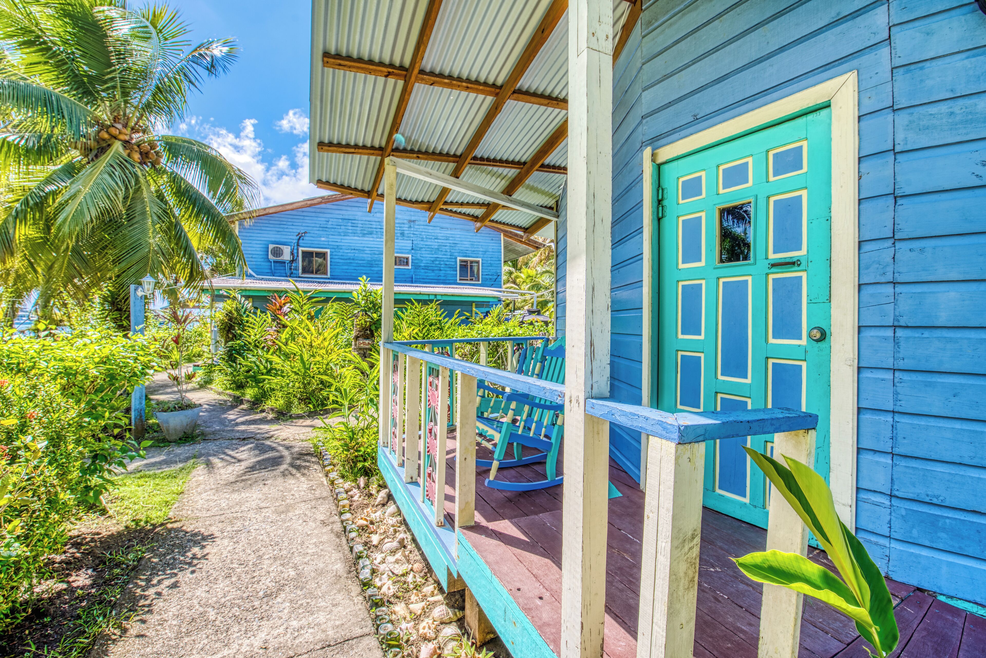 A blue house with a porch, a turquoise door, and a palm tree.