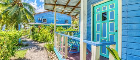 A blue house with a porch, a turquoise door, and a palm tree.