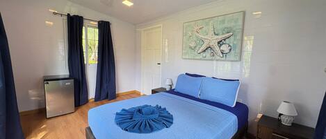 A bedroom with a bed, a small bedside table, a nightstand, a window with curtains, and a wall-mounted artwork.