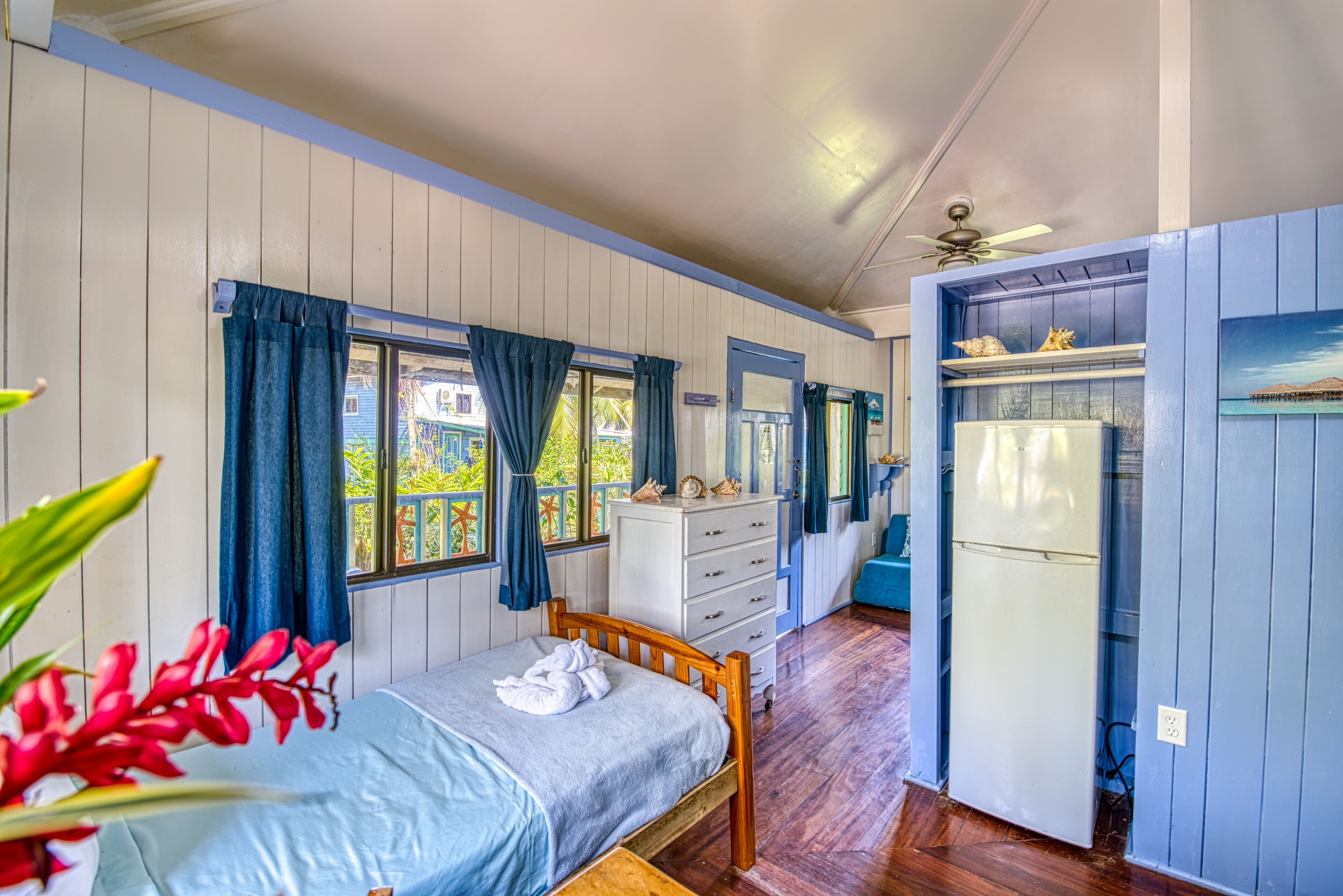 A room with a bed, a dresser, a refrigerator, and a window with curtains.