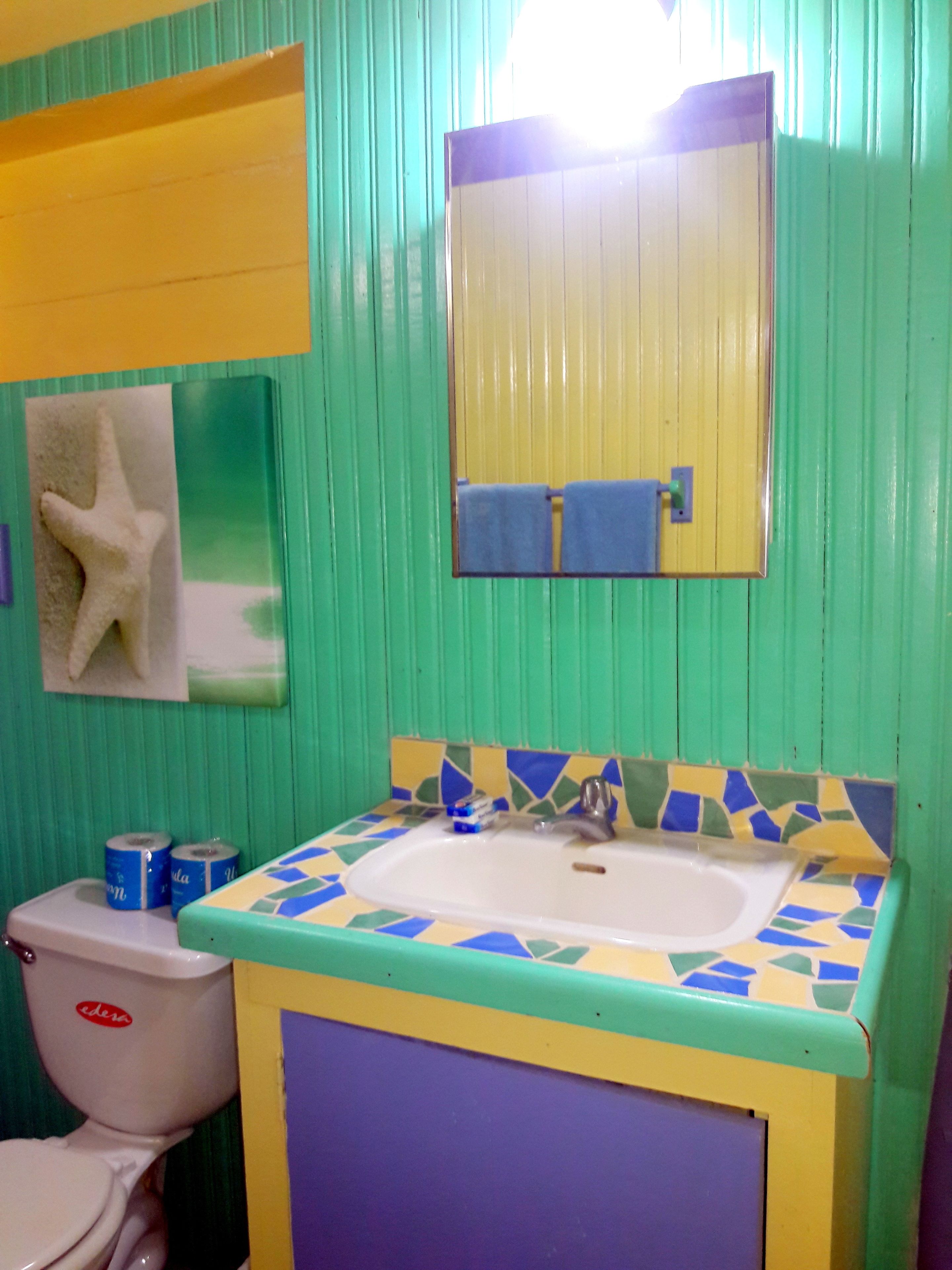 A bathroom with a green wall, a white toilet, a sink with a colorful tile backsplash, and a mirror above the sink.