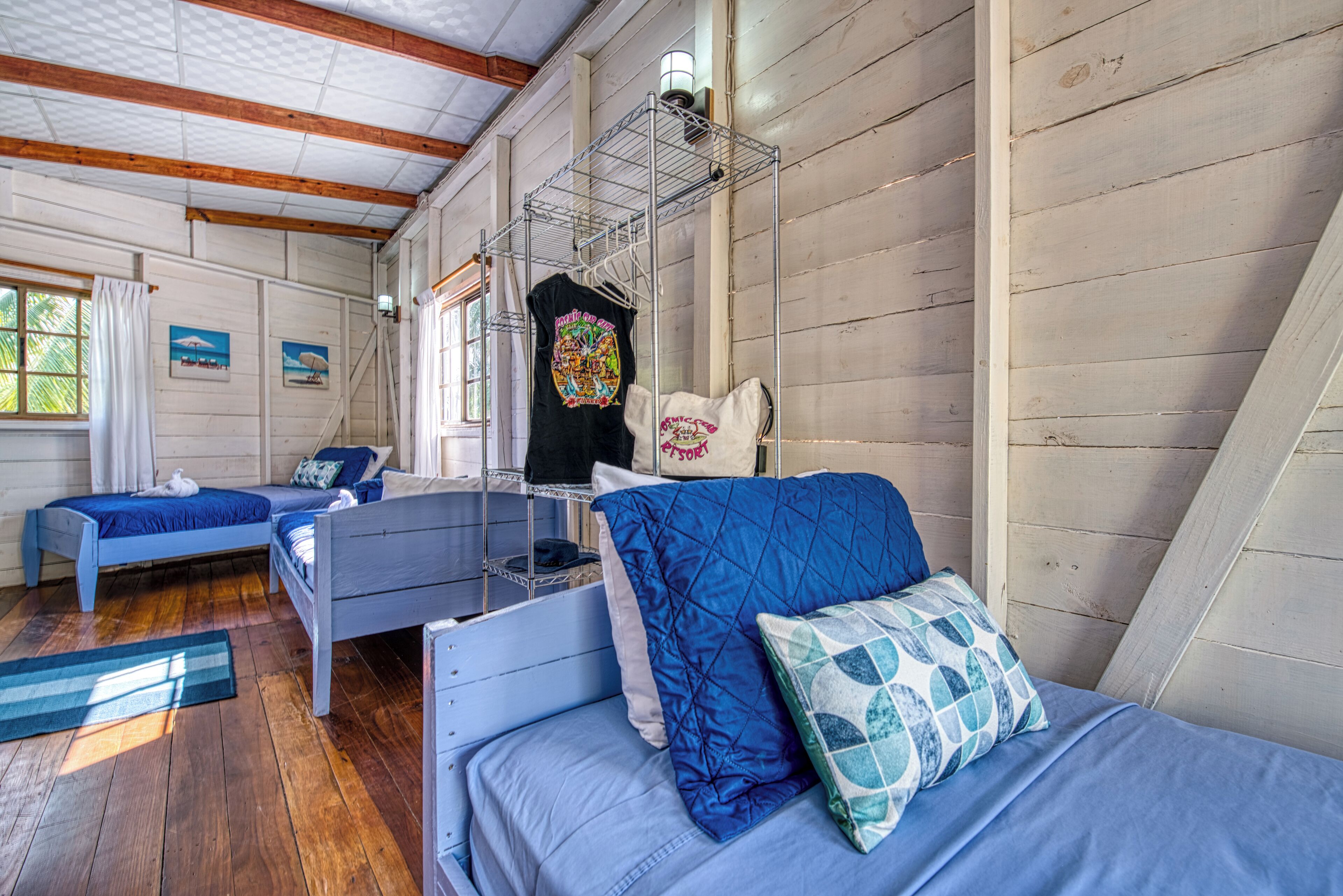 A room with two beds, a metal shelf, and a window with curtains.