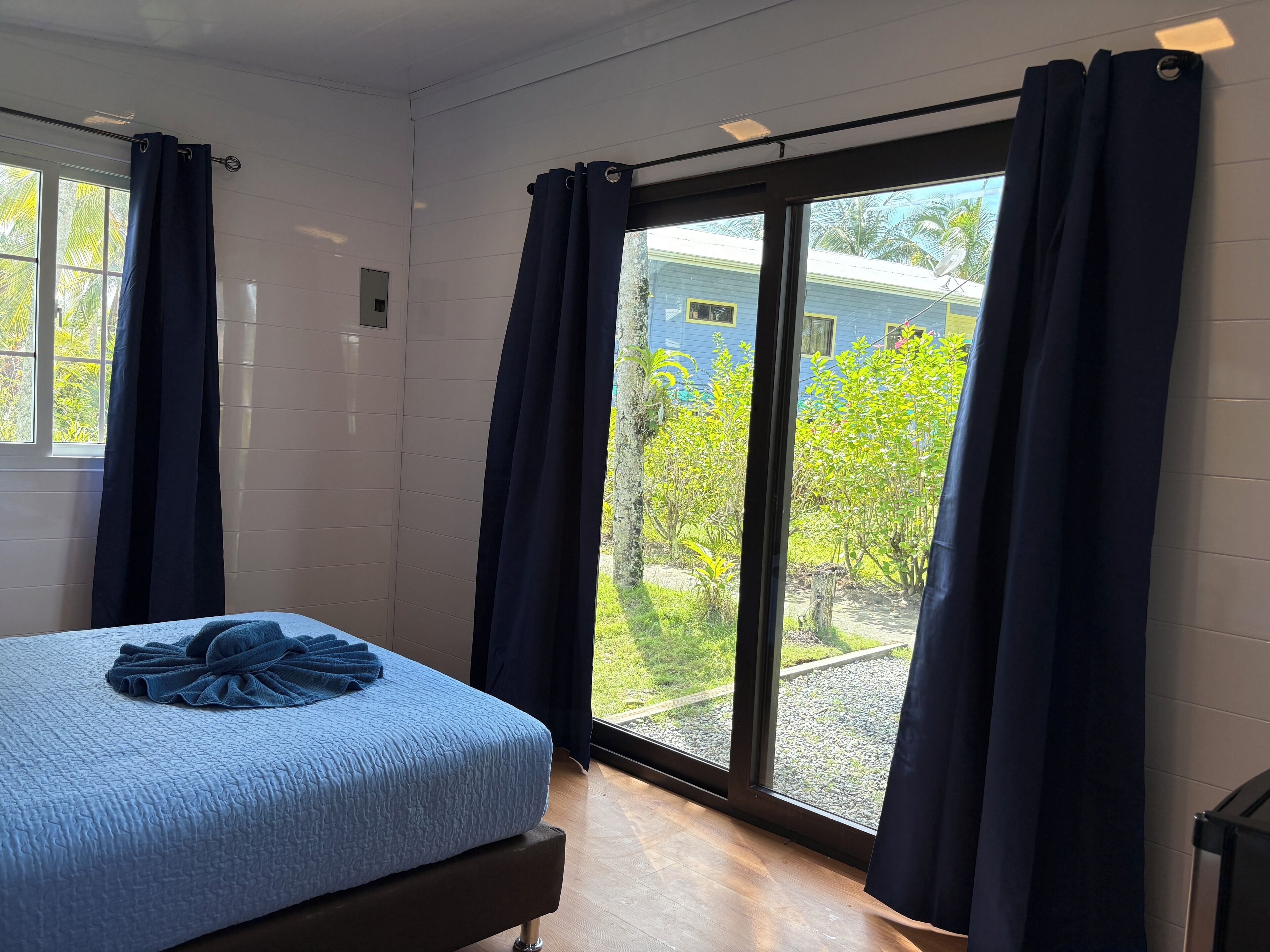 A bedroom with a bed, a window, and a view of a house and greenery outside.
