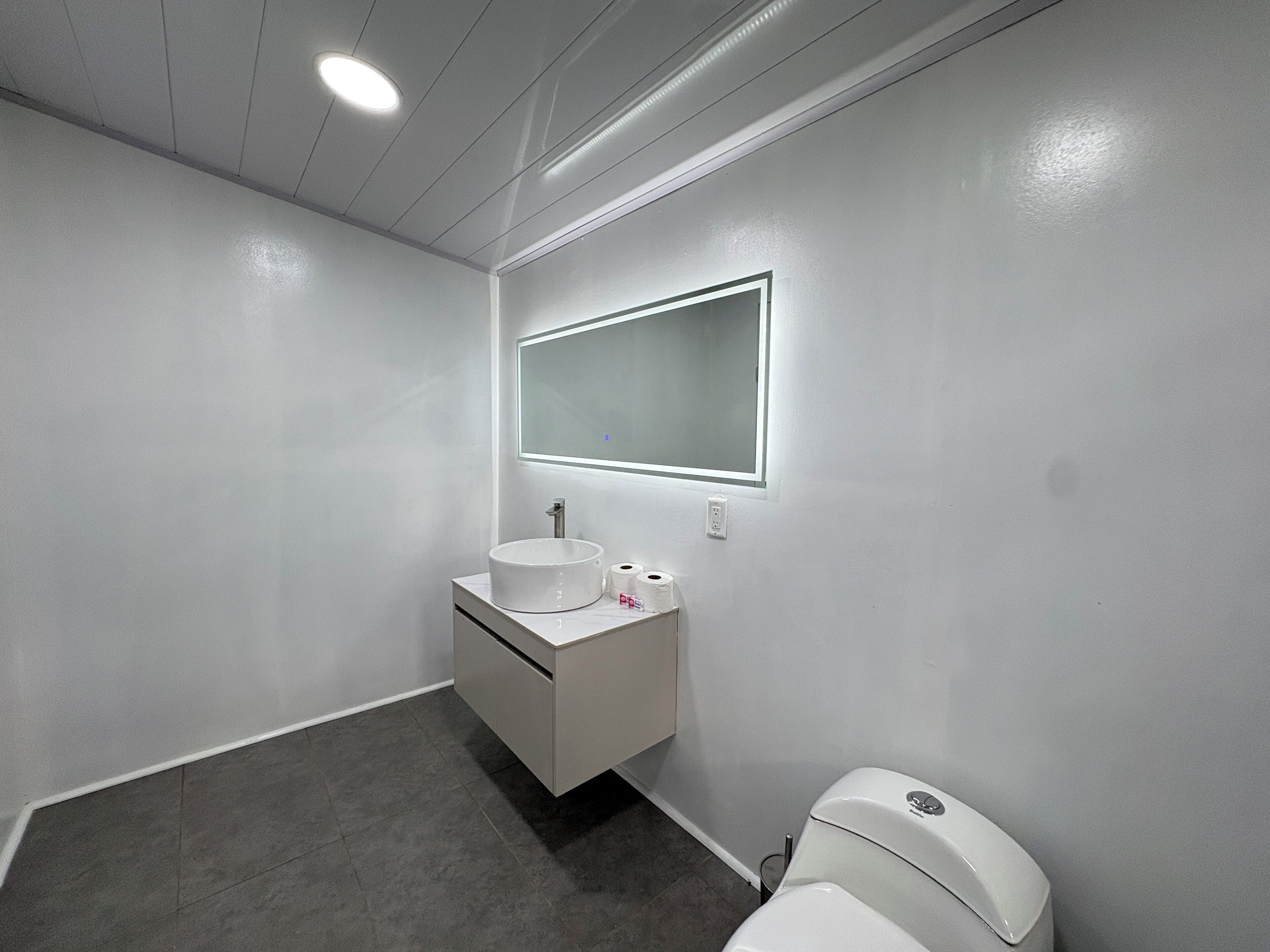A modern bathroom with a white sink, mirror, and toilet.