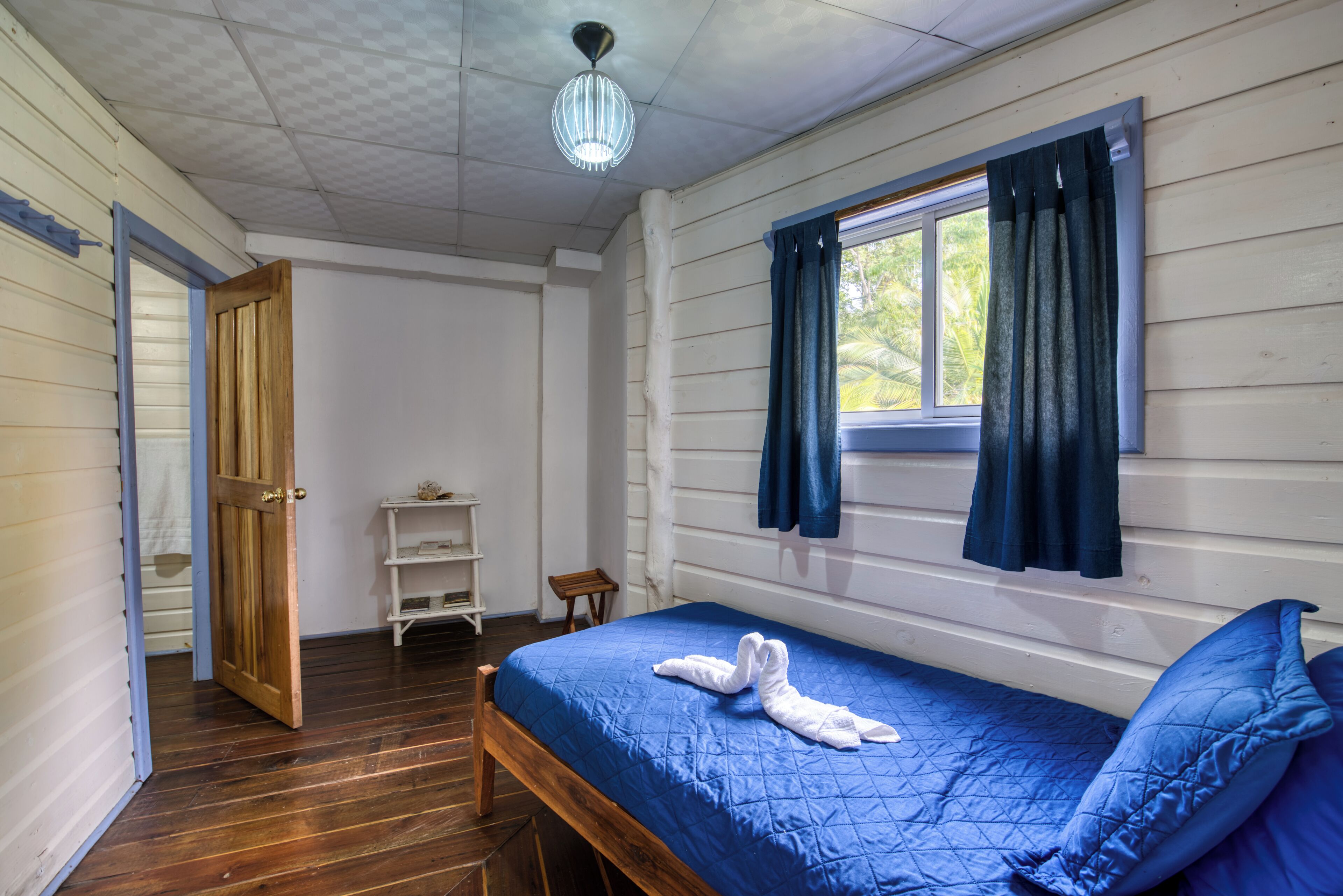 Ein Zimmer mit einem hölzernen Bett, einem Vorhangfenster, Holzboden und einer Chandelüstere.