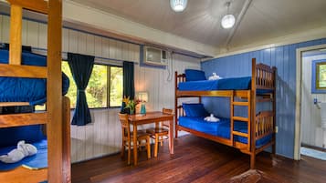 A bunk bed room with a wooden table and chairs, a window with curtains, and an air conditioning unit.