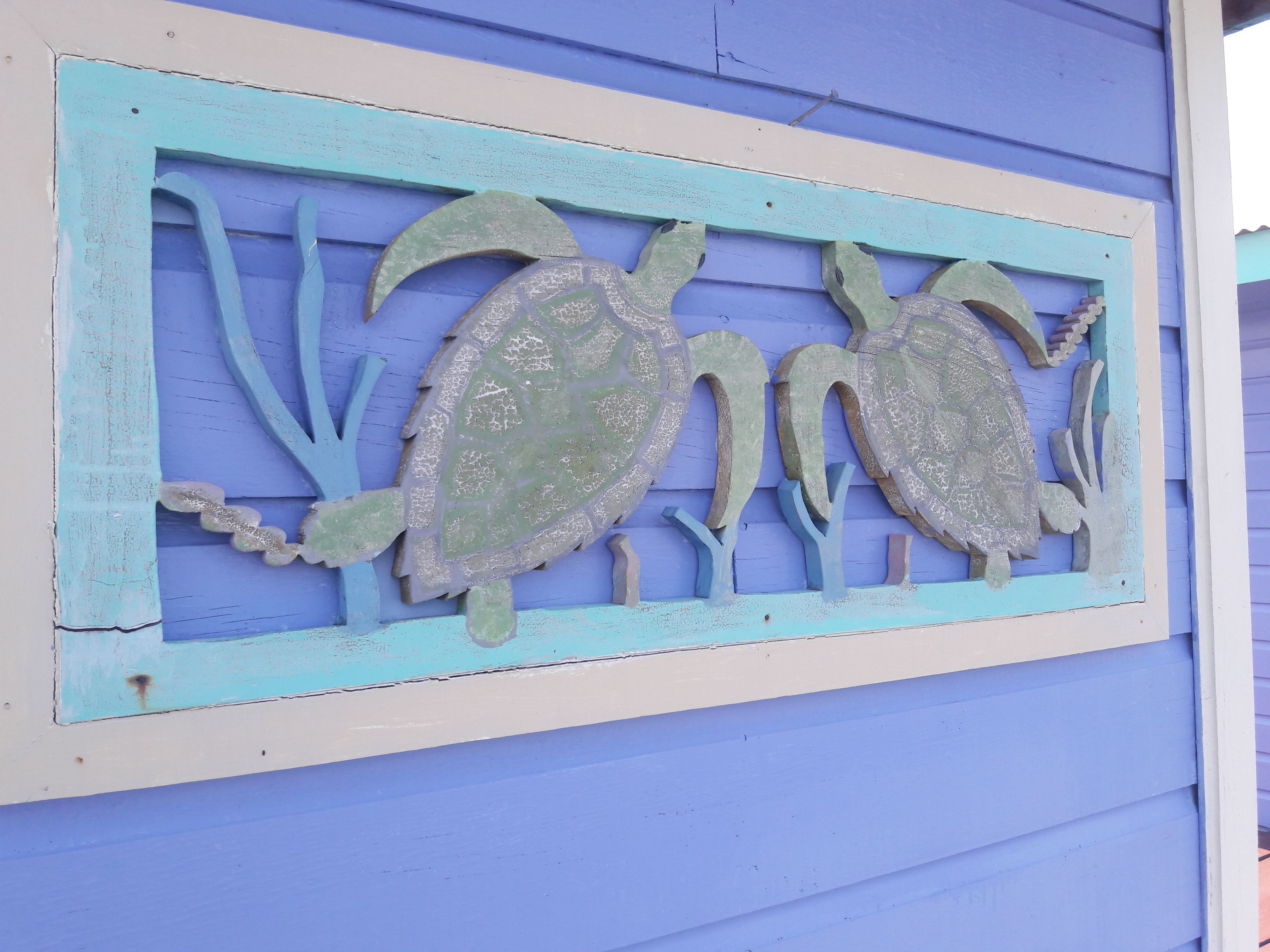 A decorative metal sign with two turtles on a blue wall.