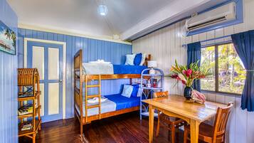 A room with bunk beds, a wooden table, chairs, a bookshelf, and a window with curtains.