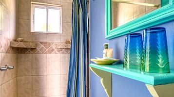 A bathroom with a white sink, a mirror, a shelf with toiletries, and a shower area.