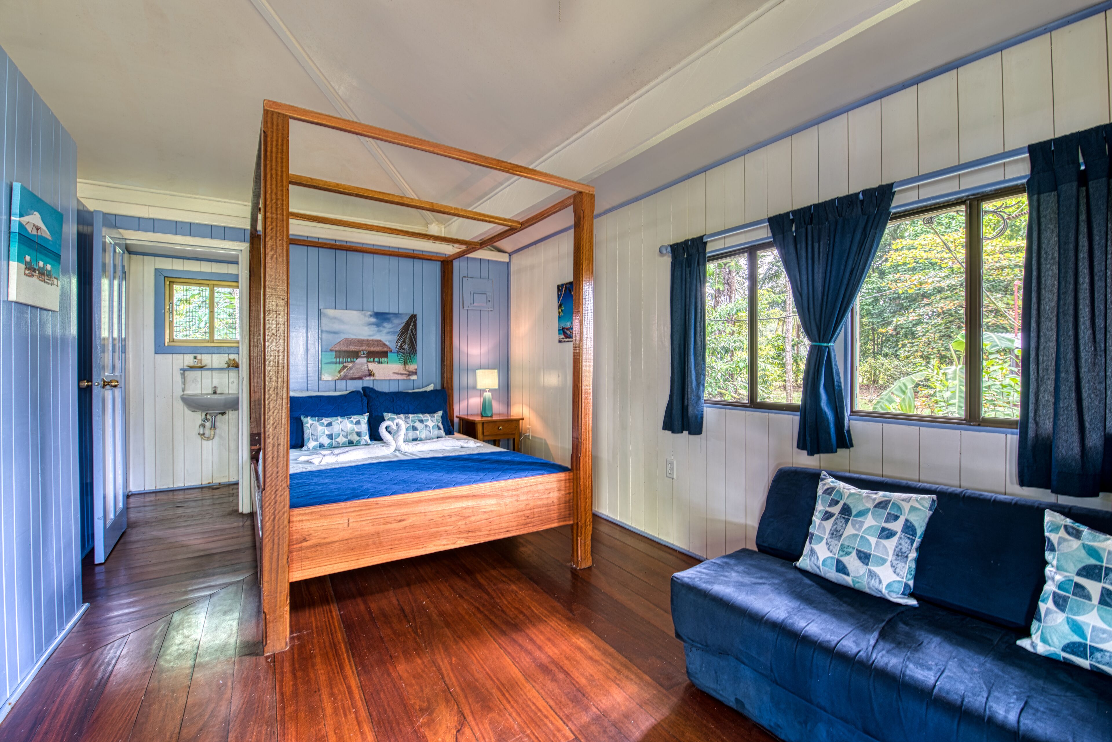 A bedroom with a four-poster bed, a blue sofa, and a view of the outdoors through a window.