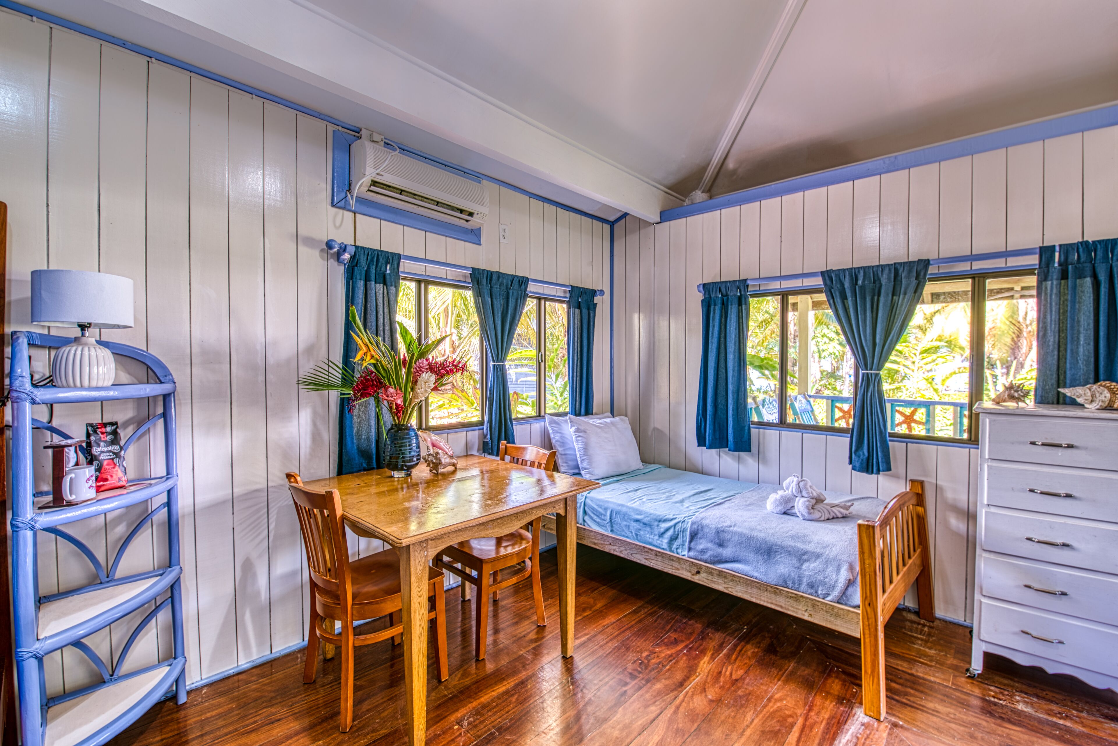 A room with a wooden table, chairs, a bed, a dresser, and a window with curtains.