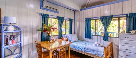 A room with a wooden table, chairs, a bed, a dresser, and a window with curtains.