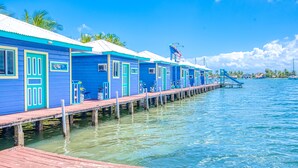 A row of blue buildings with turquoise trim, connected by a wooden dock extending into clear blue water.