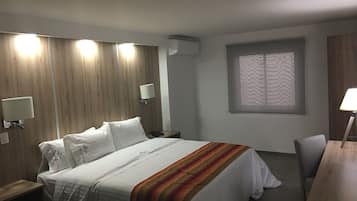 A hotel room with a large bed, bedside lamps, a desk, and a window with a patterned blind.