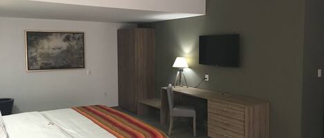 A bedroom with a bed, a desk, a chair, a television, and a wardrobe.