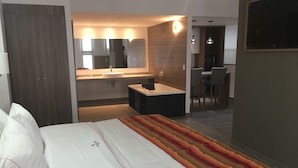 A hotel room with a bed, a bathroom with a sink and mirror, and a small desk area.