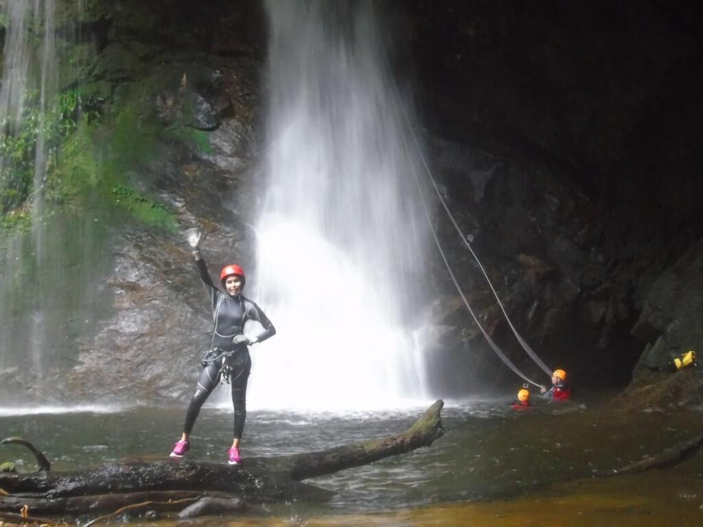 Une personne vêtue d’une combinaison de plongée, debout sur une bûche près d’une cascade.