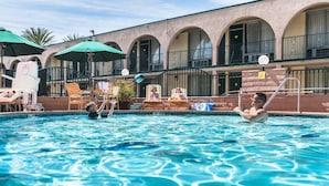 A swimming pool with lounge chairs and umbrellas, surrounded by a building with arched balconies. - Kings Inn Anaheim (Anaheim)